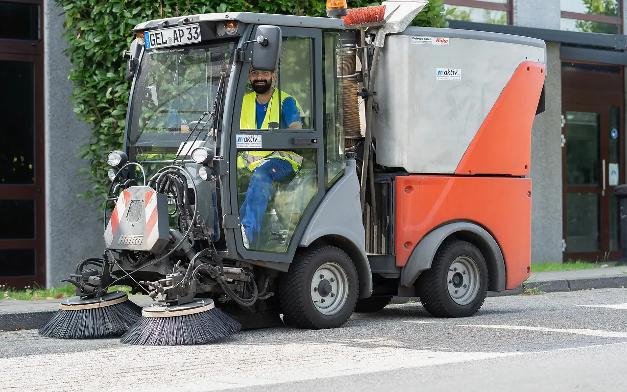 Aktiv Plus Mitarbeiter fährt Kehrmaschine für Straßenreinigung und Parkplatzreinigung